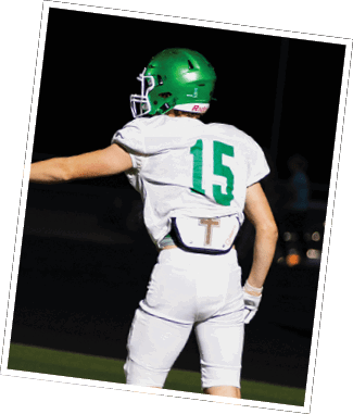 Two people wearing football helmets and uniforms are engaged in a play on a football field at night, with one person grabbing the other's jersey. Descripci n generada con IA