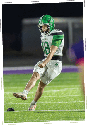 A person in sportswear is kicking a football on a green field while another person in a purple jersey with the number 45 watches from the foreground. Descripci n generada con IA