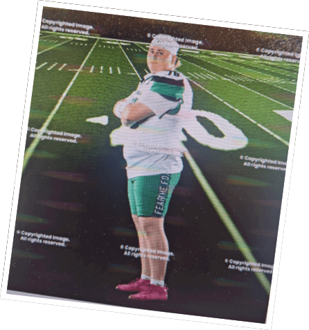A person wearing a sports uniform and pink shoes stands with arms crossed on a football field under stadium lights. Descripci n generada con IA
