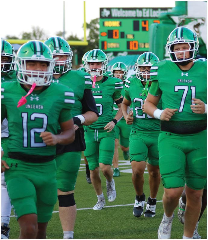 People wearing green football uniforms with helmets are running on a field. Descripci n generada con IA
