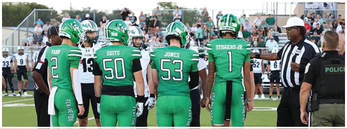 Four people in green football uniforms stand on a field facing away from the camera while two people in black and white uniforms stand opposite them. Descripci n generada con IA