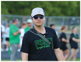 A person wearing a gray and red cap and blue sunglasses is outdoors with a blurred green background. Descripci n generada con IA