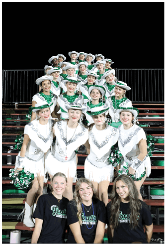 A group of people wearing white hats and green sequined outfits are smiling and posing closely together against a black background. Descripci n generada con IA