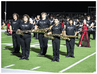 People in matching black uniforms stand on a football field holding saxophones while one person in a red and black dress stands behind them. Descripci n generada con IA