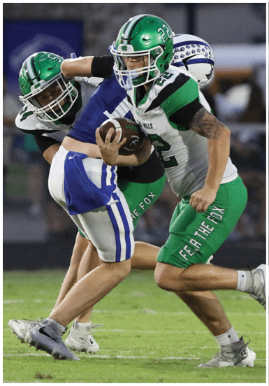 Two people in football uniforms are engaged in a play on a grassy field, with one person holding the ball and the other attempting to tackle. Descripci n generada con IA