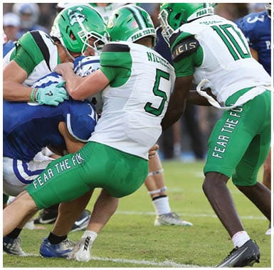 A person wearing a green football uniform with the name Reeves and number 22 is running on a football field with a referee and another player nearby. Descripci n generada con IA