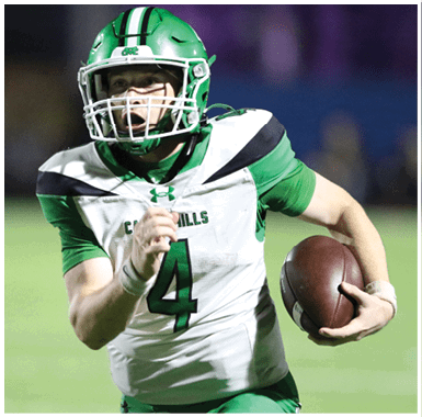 Three people in green football uniforms and helmets stand on a field at night with one person facing away from the camera and the others partially turned. Descripci n generada con IA