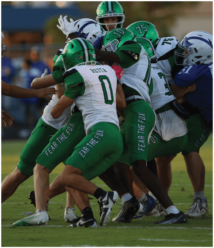 Several people in green and white sports uniforms are tightly grouped and engaged in a physical struggle with others in blue and white uniforms on a grassy field. Descripci n generada con IA