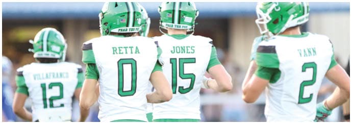 Three people wearing green and white football uniforms with helmets stand on a field, with two of the jerseys displaying the names Retta and Jones along with numbers 0 and 15. Descripci n generada con IA
