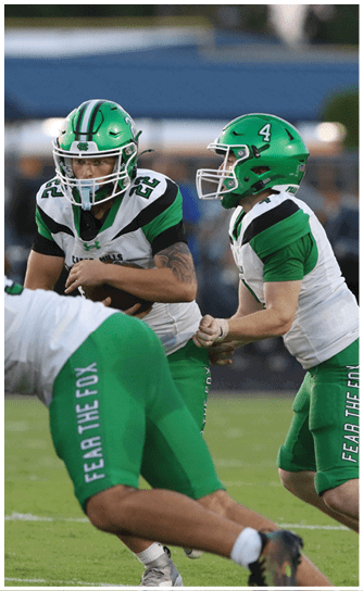 Two people in green football uniforms and helmets are engaged in a play on a football field with one person handing off the ball to the other. Descripci n generada con IA