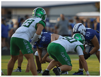 Two people in green football uniforms are crouched on a field while another person in a white and black uniform stands nearby during a game. Descripci n generada con IA