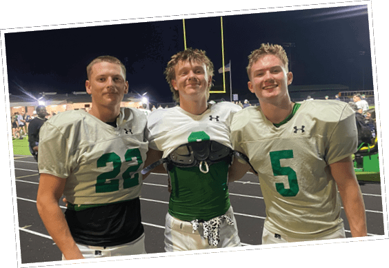 Two adults wearing football uniforms with numbers 8 and 5 are standing on a sports field at night smiling with goalposts and a flag visible in the background. Descripci n generada con IA