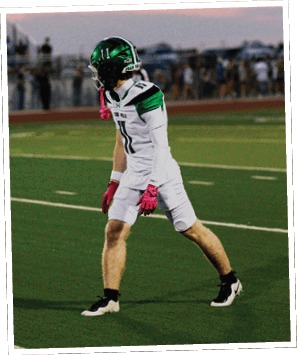 A person wearing green football pants with the words “FEAR THE FOX" printed on the side is preparing to throw a football on a turf field. Descripci n generada con IA