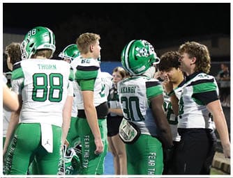 A group of people wearing green and white football uniforms are gathered on a field at night, some standing and others walking. Descripci n generada con IA