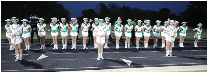 A group of people dressed in matching white and green uniforms with hats are standing in a line on an outdoor track at dusk. Descripci n generada con IA