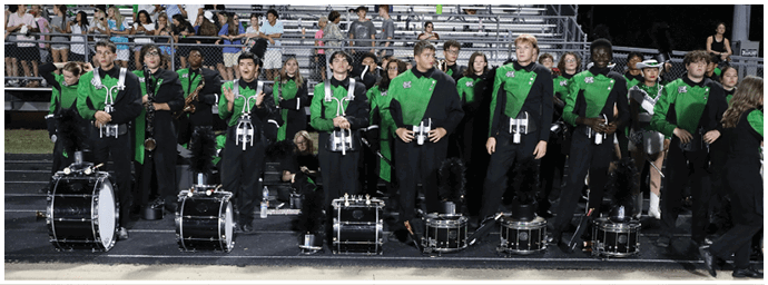 A row of four black marching band drums is placed on the ground in front of people standing on a stage or platform. Descripci n generada con IA