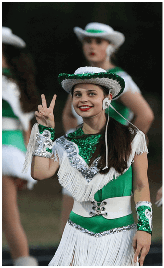 People dressed in green and white sequined costumes with fringe and hats are standing outdoors, possibly preparing for a performance. Descripci n generada con IA