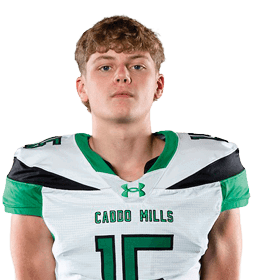 A person stands facing forward wearing a white and green sports uniform with the number 15 and the words “CYPRESS MILLS" on the jersey. Descripci n generada con IA
