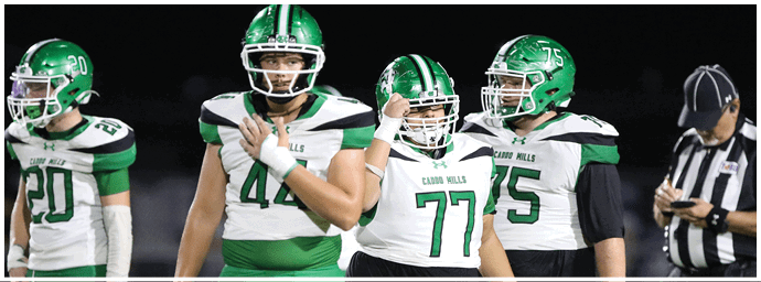 A group of people wearing green football uniforms and helmets are gathered on a field with two adults in black coaching attire standing among them. Descripci n generada con IA
