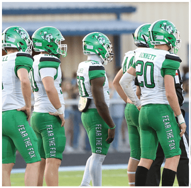Four people in green and white football uniforms with helmets stand on a field next to a referee in black and white stripes. Descripci n generada con IA