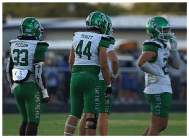 A group of people wearing green and white football uniforms are lined up on a grassy field, preparing for a play during a game. Descripci n generada con IA