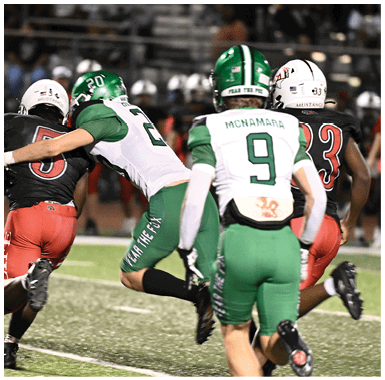 Two people in green and white football uniforms are engaged in a play on a football field with one person tackling an opponent in a black and red uniform. Descripci n generada con IA