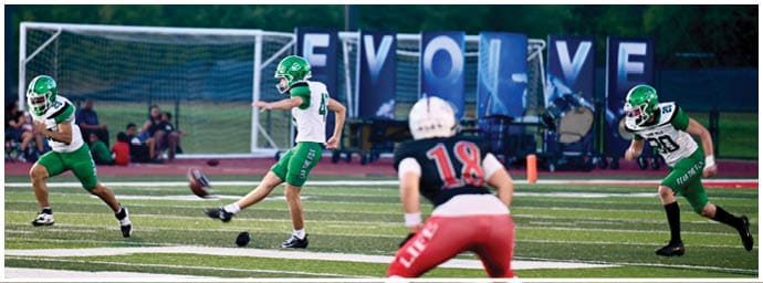 Four people wearing green and white football uniforms stand on a field with a blurred background of spectators and a referee nearby. Descripci n generada con IA
