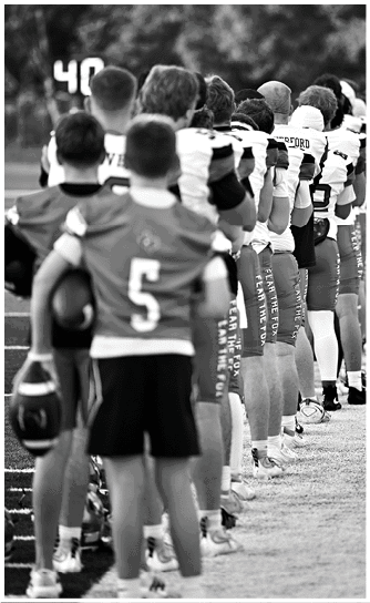 A line of people wearing sports uniforms stand closely together facing away from the camera with a blurred natural background. Descripci n generada con IA