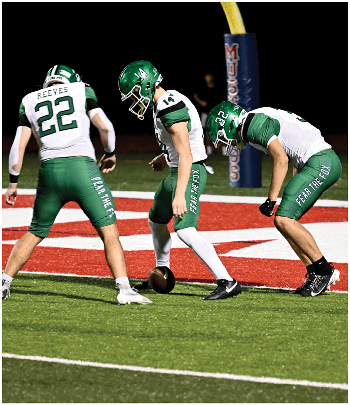 Two people in green and white football uniforms with helmets are preparing to play on a red and white field near a goalpost. Descripci n generada con IA