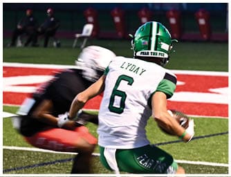A person wearing a green and white football uniform with the name Lyday and number 6 is running on a field while another person in a black and red uniform is approaching. Descripci n generada con IA