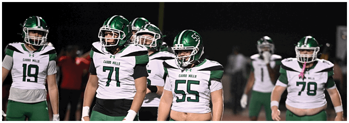 Five people wearing green and white football uniforms with helmets are standing on a field at night. Descripci n generada con IA