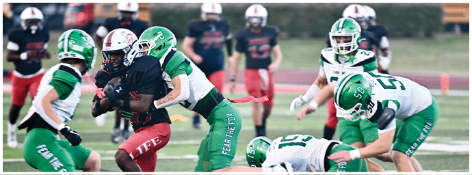 People wearing football helmets and uniforms are engaged in a tackle on a football field during a game. Descripci n generada con IA