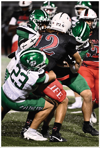 Several people in football uniforms are engaged in a close tackle during a game on a grassy field. Descripci n generada con IA