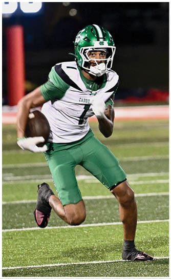 A person wearing a green and white football helmet and uniform is focused and appears to be in motion during a nighttime game. Descripci n generada con IA