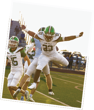 Two people in football uniforms celebrating on a field with one person jumping in the air and another person reaching out. Descripci n generada con IA