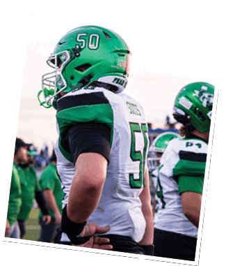 People wearing green and white football uniforms and helmets stand on a field, appearing to watch or prepare for a game. Descripci n generada con IA