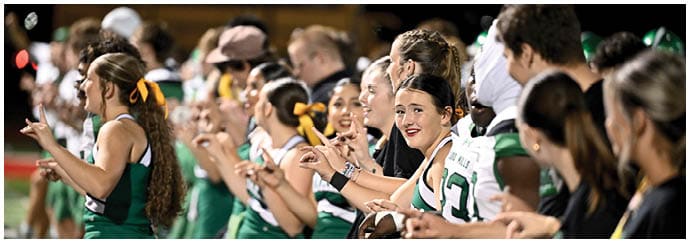A group of people in green and white sports uniforms are standing closely together, smiling and pointing in the same direction. Descripci n generada con IA