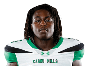 A person stands facing forward wearing a white and green football uniform with the number 33 and the words “Cedar Hills" on the jersey. Descripci n generada con IA