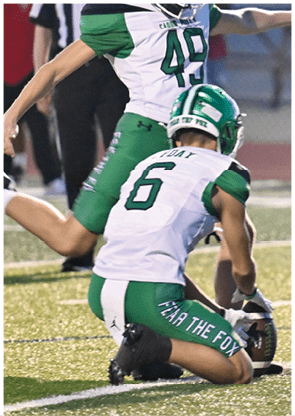 Two people in green and white football uniforms are on a field, with one person wearing a helmet and the other jumping behind them. Descripci n generada con IA