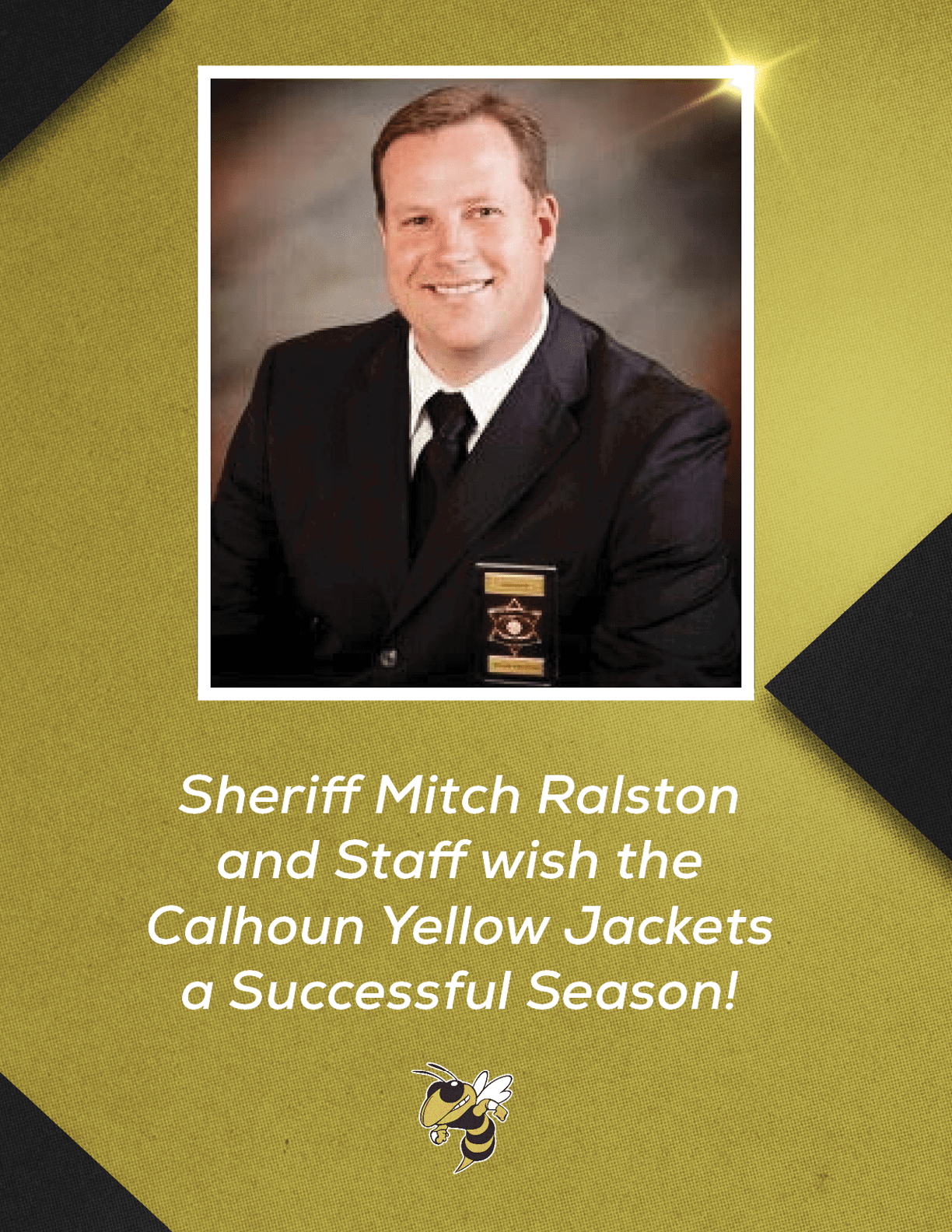 A person in a dark suit with a badge smiles against a neutral background above text wishing the Calhoun Yellow Jackets a successful season with a small yellow jacket mascot below. Description generated by AI
