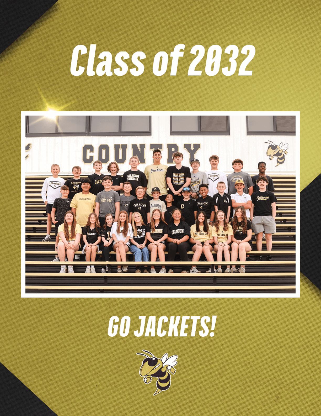 A group of children wearing black and yellow shirts is seated and standing on bleachers in front of a wall with the word “COUNTRY" and a yellow jacket mascot, with text above and below the group reading "Class of 2032" and "GO JACKETS!" respectively. Description generated by AI
