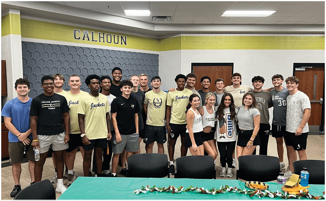 A group of people wearing casual clothing are gathered indoors in front of a banner that reads “Seniors Class of 2023" with tables and chairs in the foreground. Description generated by AI