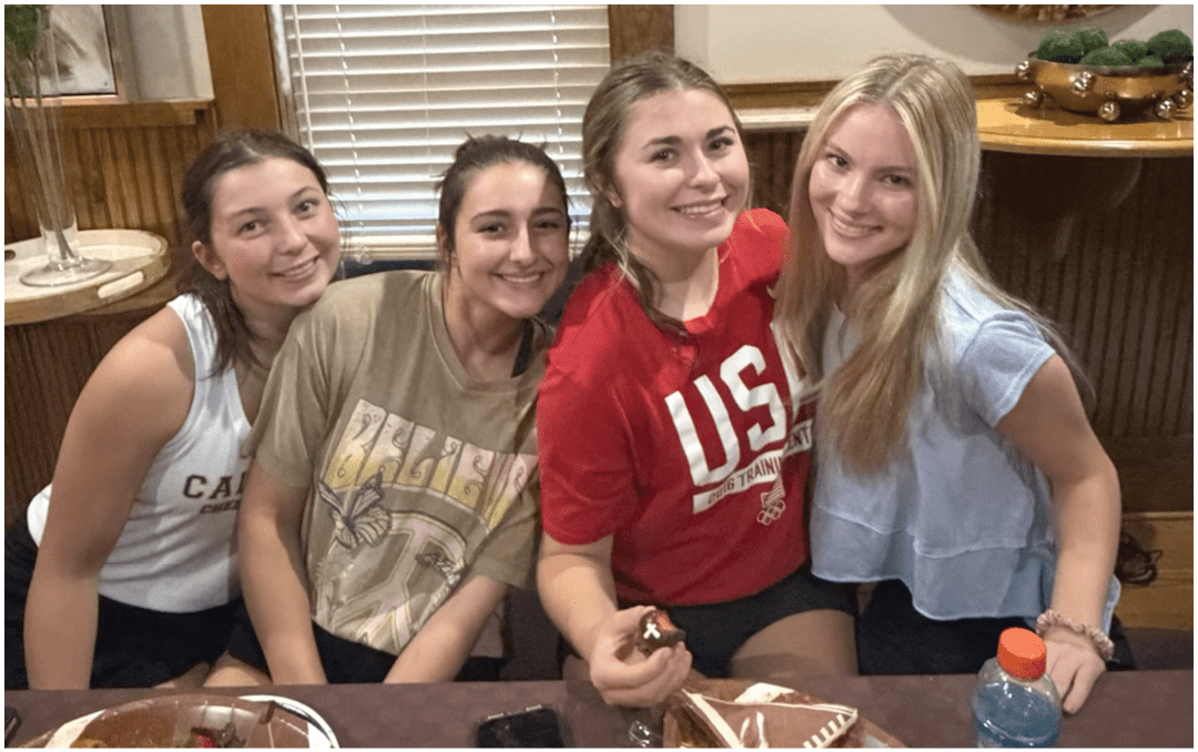A group of people sitting around a long dining table in a room with a high wooden ceiling and a banner that reads “Seniors Class of 2023" while eating and talking. Description generated by AI
