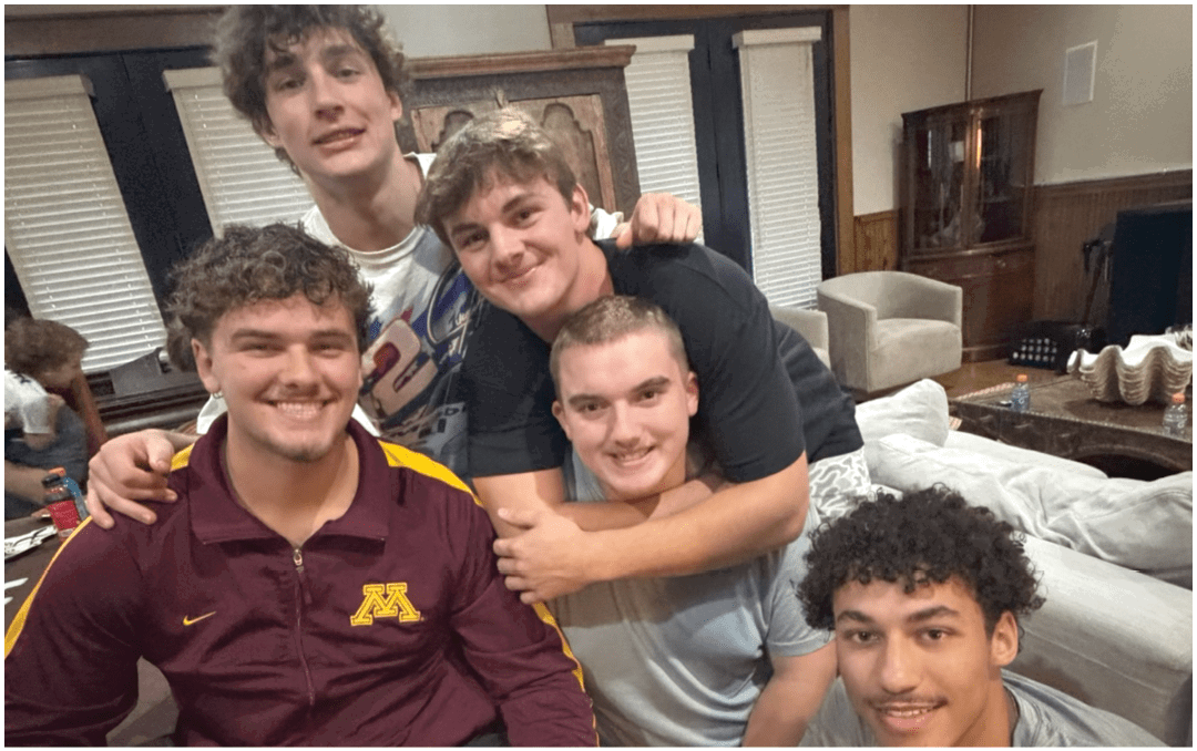 A group of people sitting around a long dining table in a room with a high wooden ceiling and a banner that reads “Seniors Class of 2023" while eating and talking. Description generated by AI
