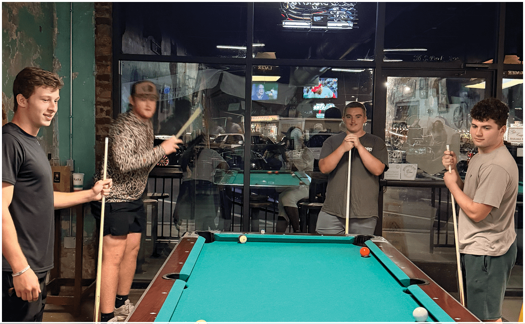 A group of people sitting and standing around tables in a room with a “Seniors Class of 2023" banner, eating and socializing. Description generated by AI
