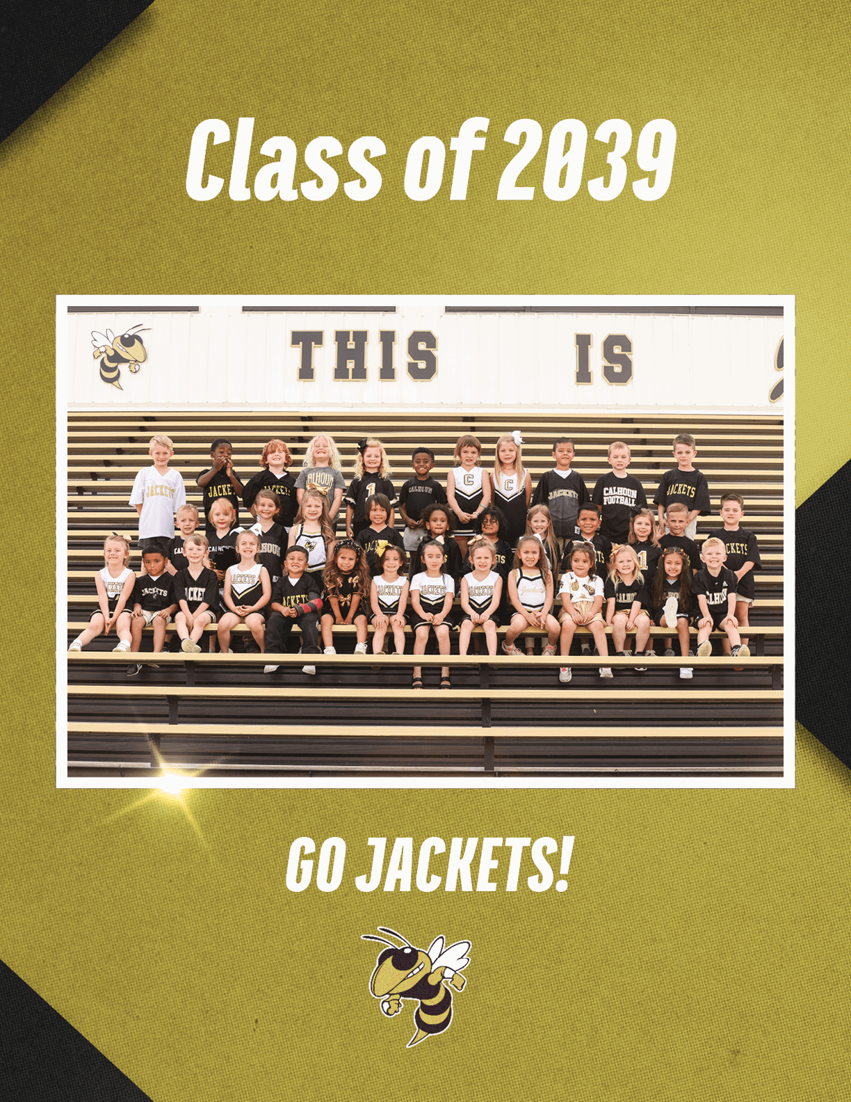 A group of children wearing black and white sports-themed clothing are seated on bleachers under a sign that reads “THIS IS" with text above saying "Class of 2039" and below saying "GO JACKETS!" along with a yellow jacket mascot illustration. Description generated by AI