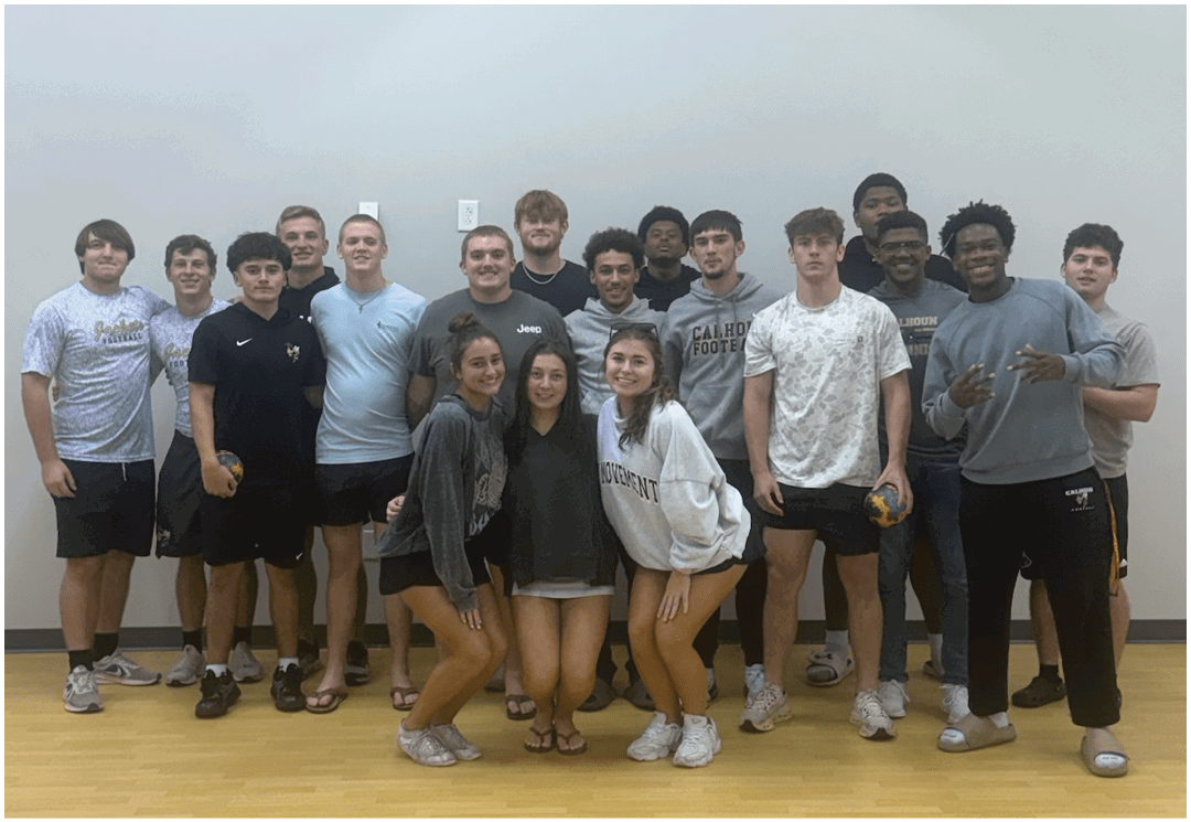 A group of people wearing casual clothing are gathered indoors in front of a banner that reads “Seniors Class of 2023" with tables and chairs in the foreground. Description generated by AI