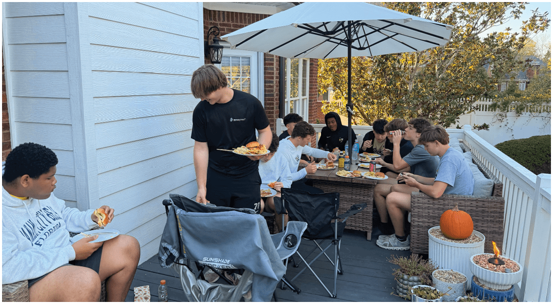 A decorated table with trophies and gift bags is set up below a large screen displaying a group photo of a football team on a field. Description generated by AI