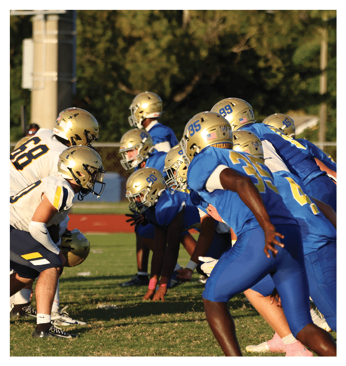 A football game is in progress with players on the field. One player is throwing a football while another player is trying to catch it. The players are wearing uniforms and are actively engaged in the game. AI generated content