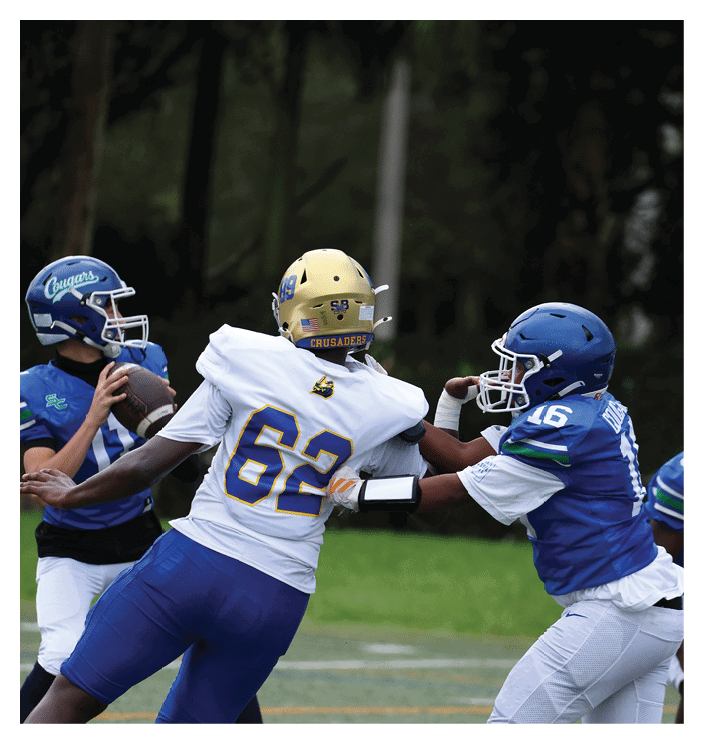 A football game is in progress with players on the field. One player is throwing a football while another player is trying to catch it. The players are wearing uniforms and are actively engaged in the game. AI generated content